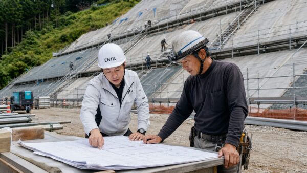 現場の片隅で図面を広げて打ち合わせをしている日本人の現場監督と法面職人