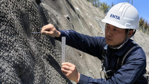 吹付モルタル法面の厚さを検尺ピンで測定している